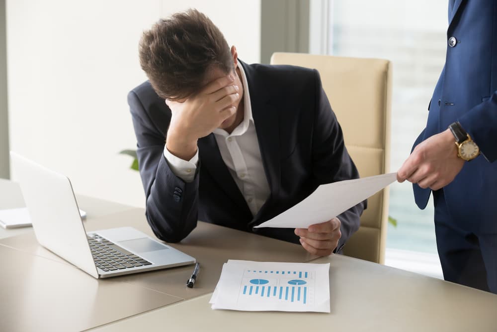 Disheartened manager receives a dismissal notice, sitting at a desk with a laptop and financial documents—upset by bad news and business failure.